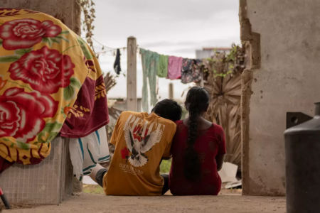 The backs of a young man and a young woman sitting on the doorstep of a house.