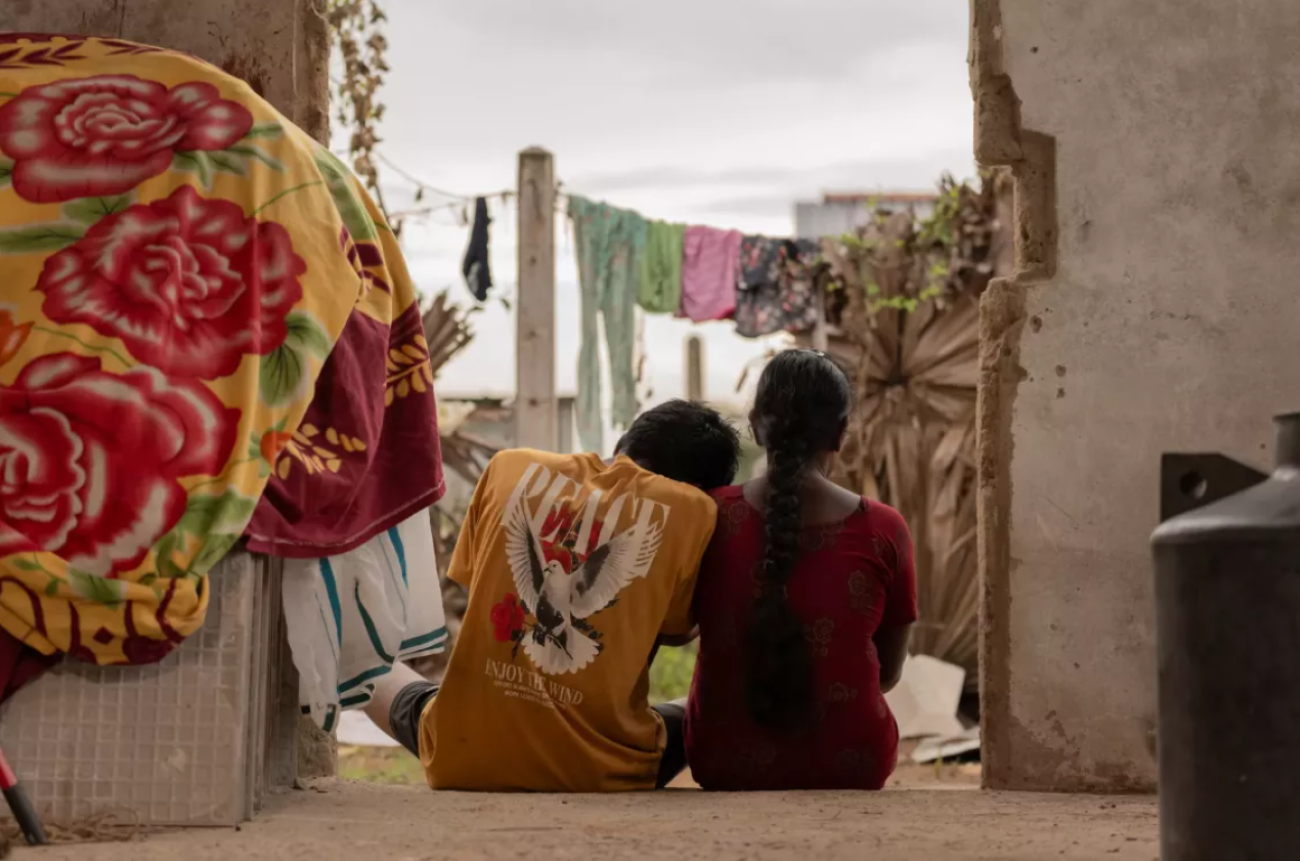 The backs of a young man and a young woman sitting on the doorstep of a house.